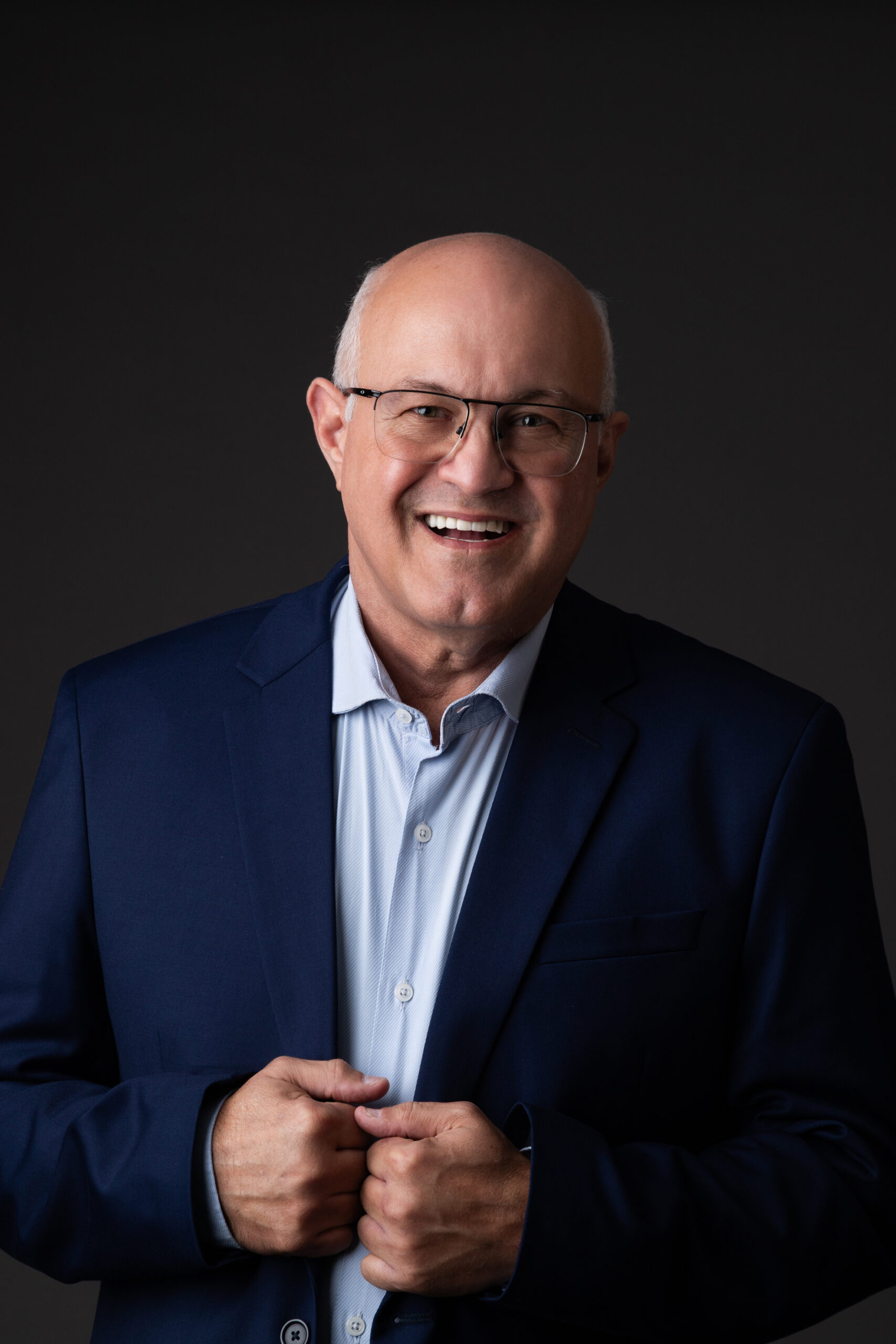 Retrato do Prof. Alexandre Amaral, neurocirurgião funcional, sorrindo e vestido com blazer azul em fundo escuro.